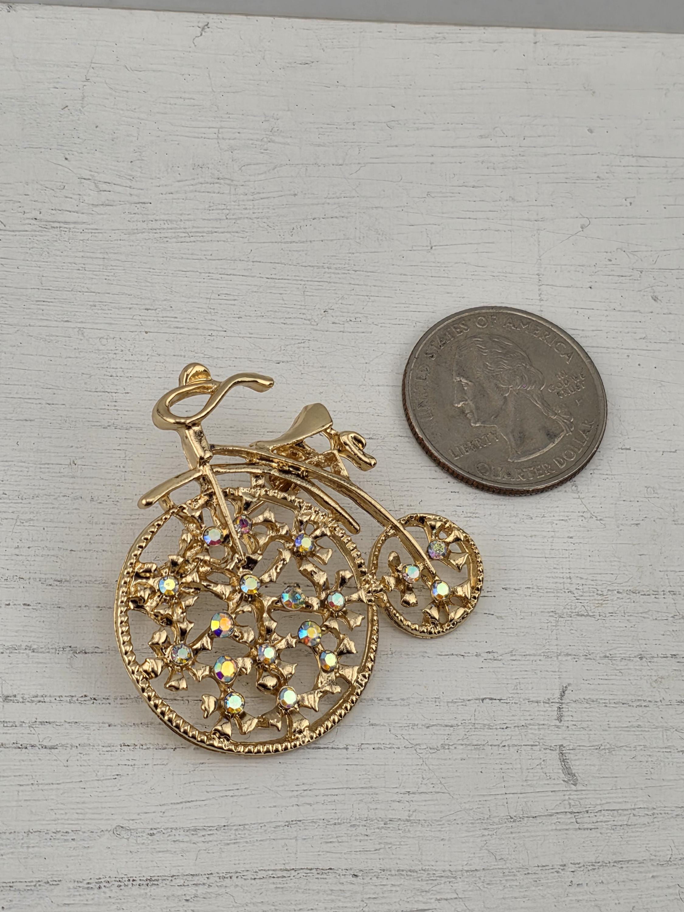 A gold-colored brooch with a floral design and a small coin placed next to it on a white surface.