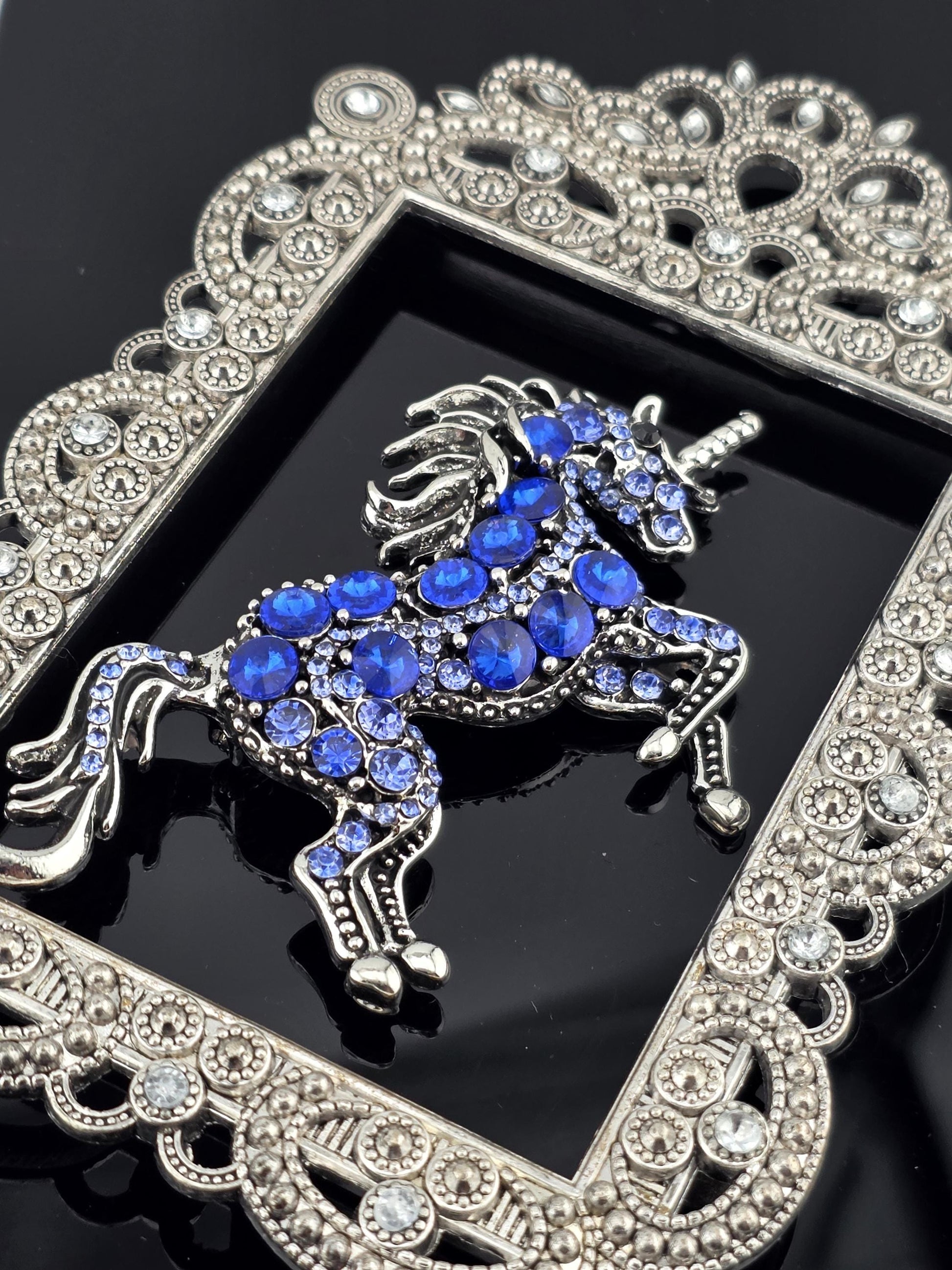 A silver and blue ornate brooch with a detailed design, featuring a central blue gem surrounded by smaller blue gemstones.