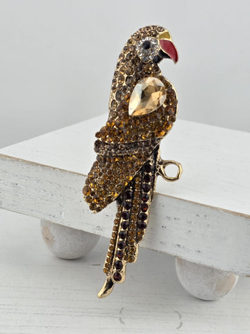 A decorative bird-shaped brooch with a gold and beige color scheme, adorned with numerous small gemstones.