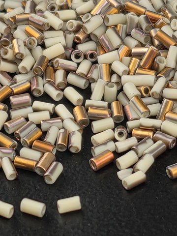 a close-up view of a pile of small, white and gold beads scattered on a dark surface.