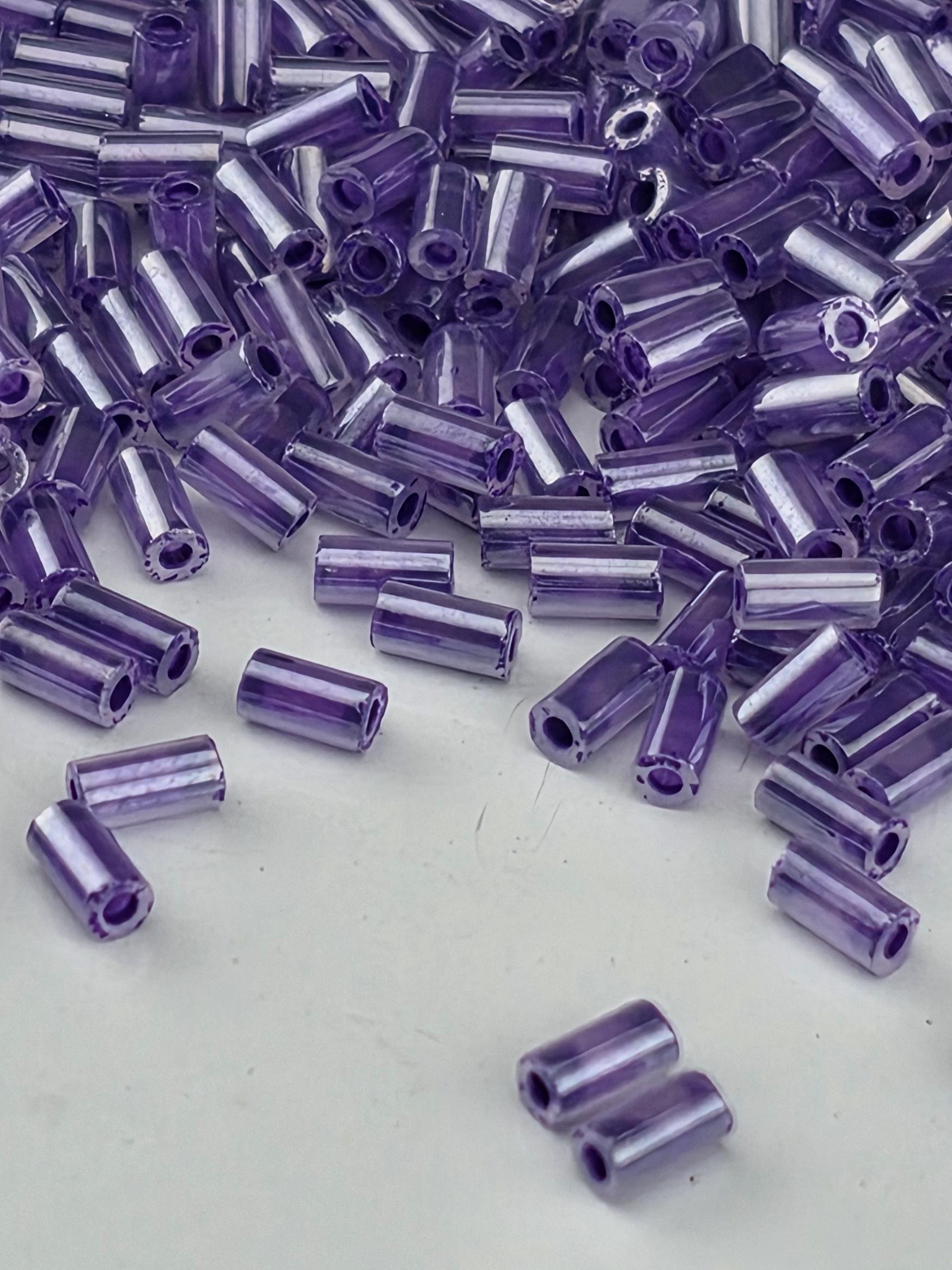 a close-up view of numerous small, clear beads in various shades of purple, scattered across a white surface.
