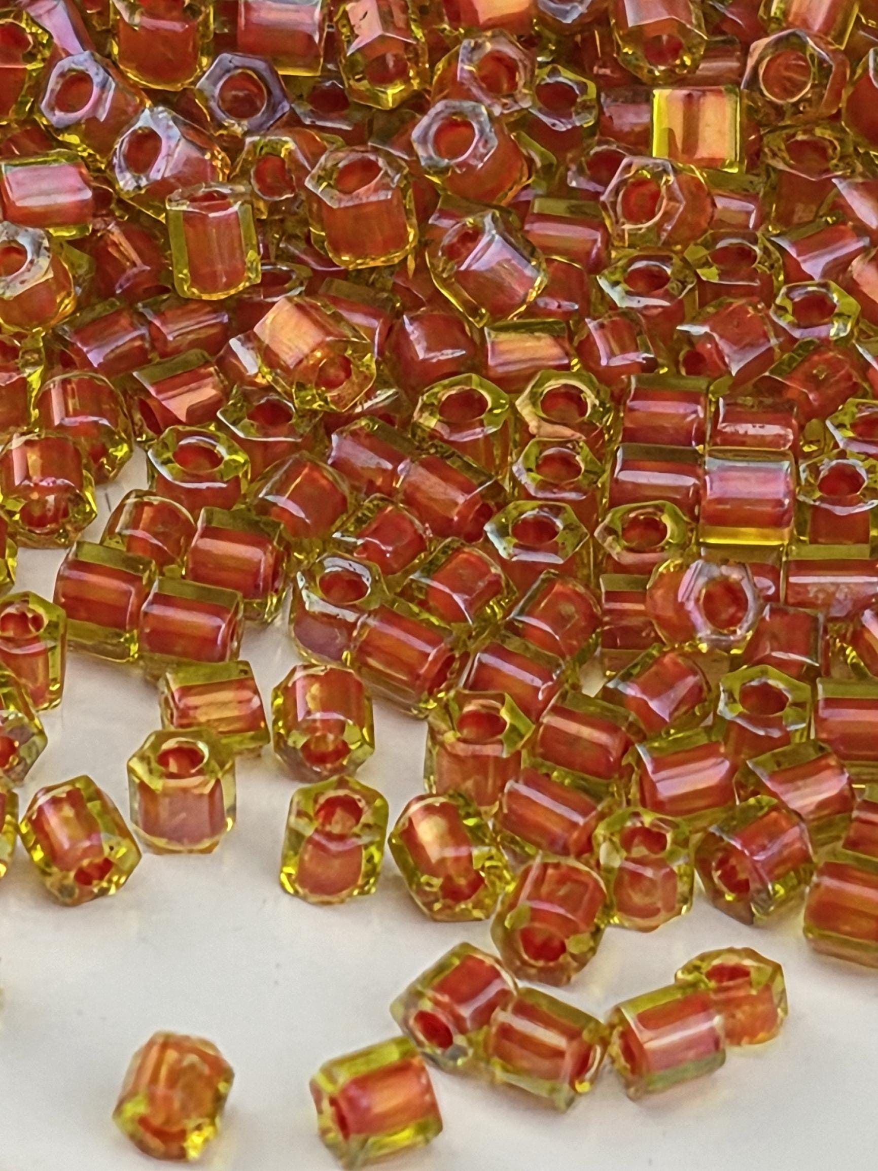 The image is a close-up of numerous small, colorful beads in shades of red and yellow, scattered across a surface.