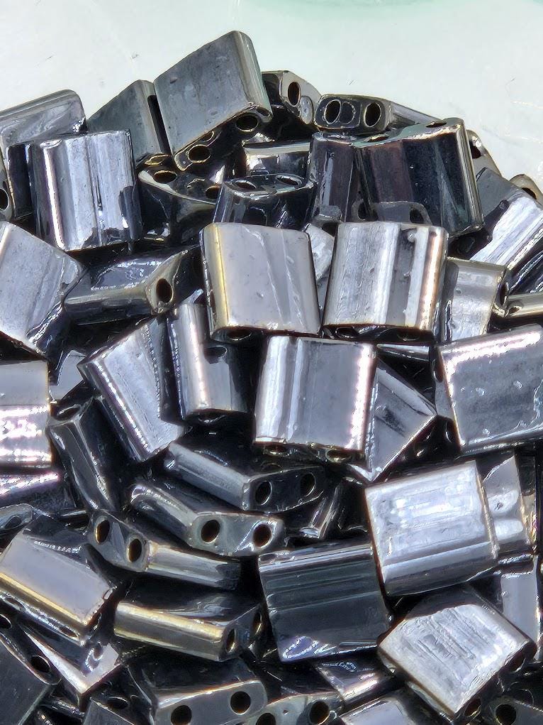 numerous metallic beads or pieces, likely made of a shiny, metallic material. The beads are scattered and overlapping, creating a visually interesting and textured composition.