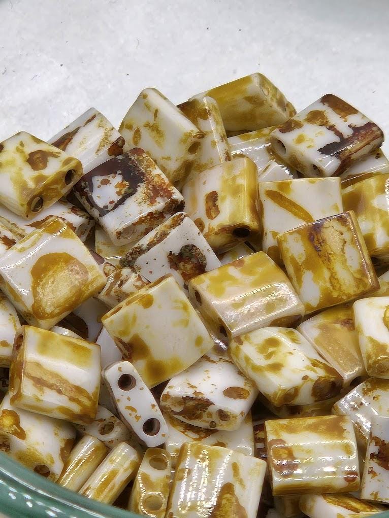 a close-up view of a pile of small, square-shaped objects with a yellow and white color pattern. The objects appear to be made of a material that resembles beads or small stones, and they are scattered together in a pile.