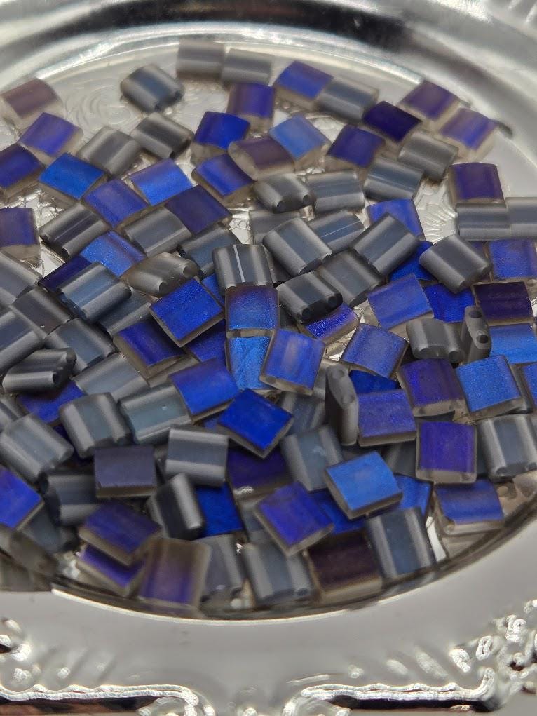 a close-up view of a silver plate filled with small, square-shaped blue and gray glass pieces.