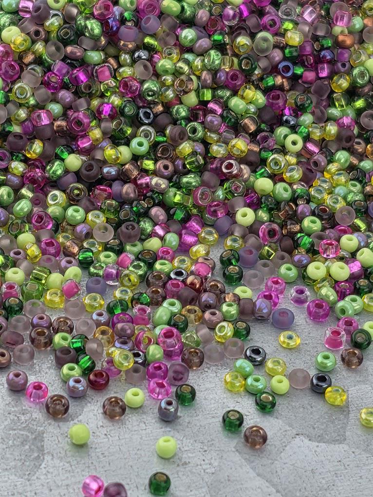 A colorful assortment of multicolored beads, including various shades of green, purple, pink, and yellow, scattered across a surface.