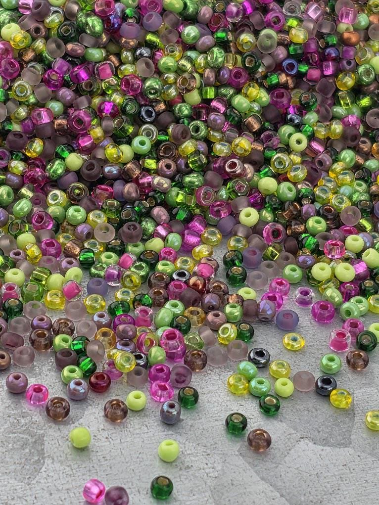 A colorful pile of multicolored beads, including various shades of green, purple, pink, and yellow, scattered across a surface.