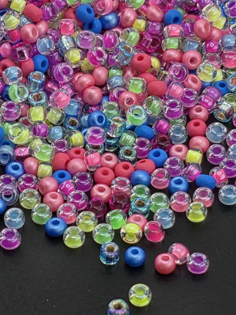 A colorful pile of multicolored plastic beads, including clear, blue, pink, and yellow beads, scattered on a dark surface.