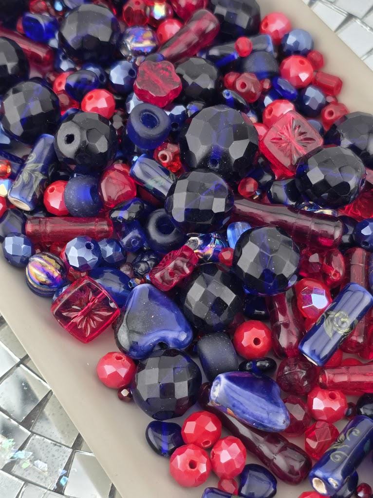 The image is a collection of various colorful beads, including red, blue, and black beads, scattered together.