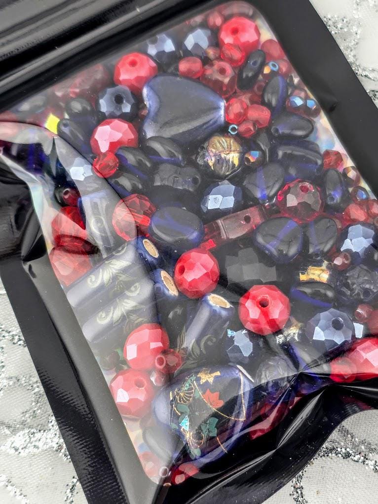 A clear plastic bag filled with a variety of colorful beads, including red, blue, and black beads, creating a visually appealing and vibrant display.