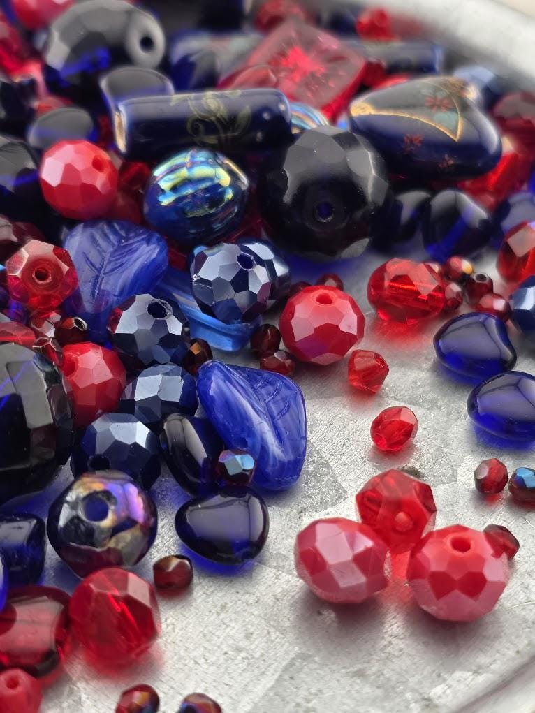 The image is a close-up of various colorful beads, including red, blue, and black beads, scattered on a surface.