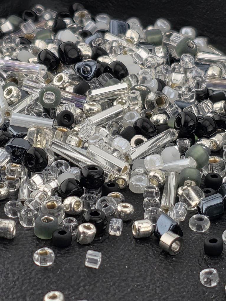 The image is a collection of various glass beads and glass rods scattered on a surface, with a mix of clear, black, and silver colors.