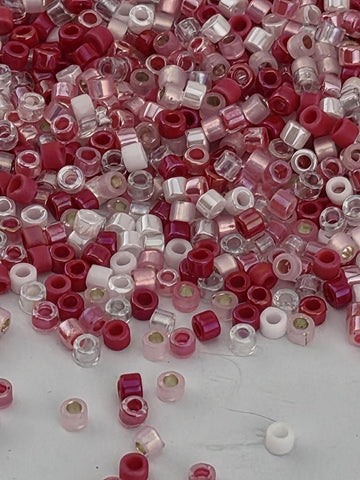 The image is a collection of various colored beads, including red, white, and clear beads, scattered across a surface.
