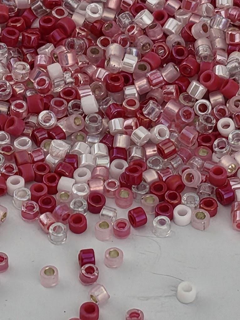 The image is a collection of various colored beads, including red, white, and clear beads, scattered across a surface.