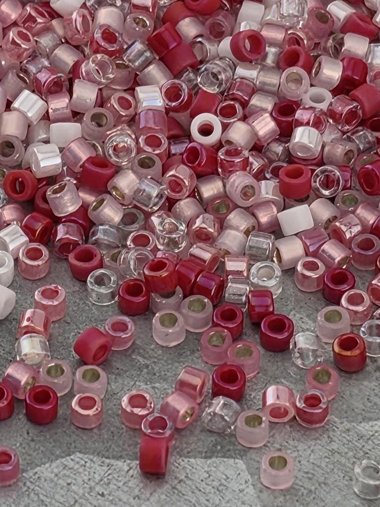 The image is a collection of various colored beads, including red, pink, and clear beads, scattered on a surface.