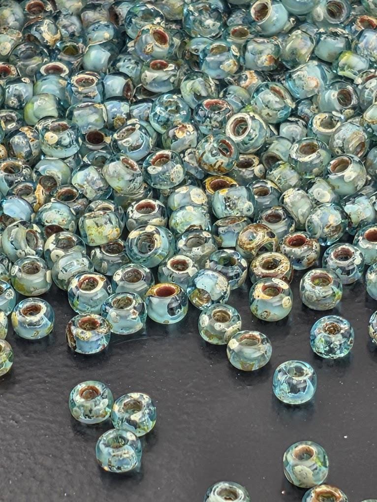 a large pile of small, blue glass beads scattered on a white surface.