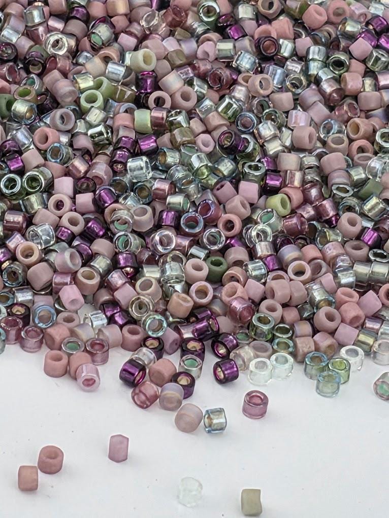 The image is a collection of various colored beads, including pink, purple, and green, scattered across a white surface.