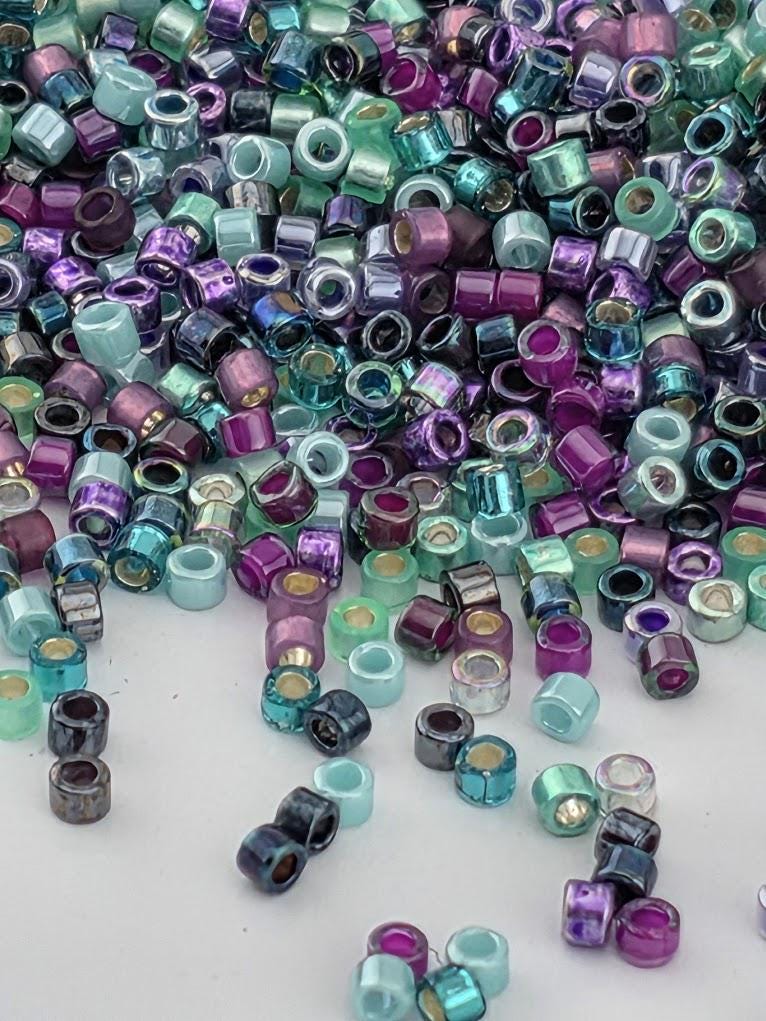 A colorful pile of multicolored beads, including shades of purple, blue, green, and turquoise, scattered across a white surface.