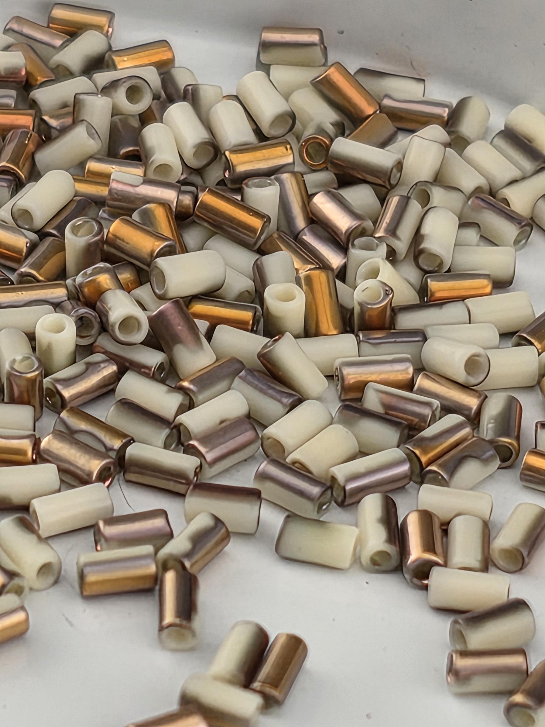 a collection of small, cylindrical objects with a mix of white, brown, and gold colors. The objects appear to be made of metal and are scattered across a surface.
