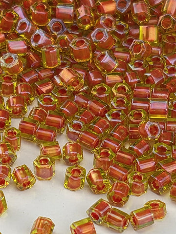 The image is a close-up of numerous small, colorful beads in shades of red and yellow, scattered across a surface.