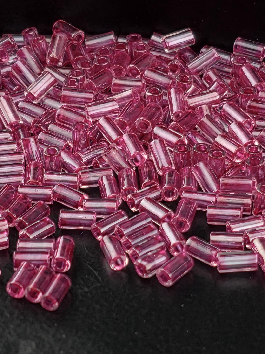 A close-up image of numerous small, clear beads in a vibrant shade of pink, scattered across a dark background.
