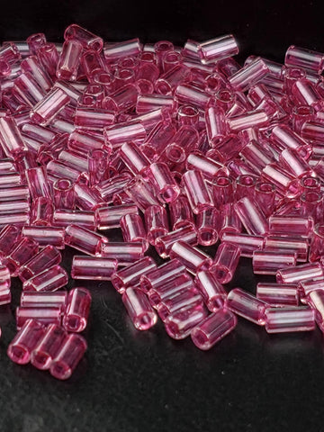 A close-up image of numerous small, clear beads in a vibrant shade of pink, scattered across a dark background.