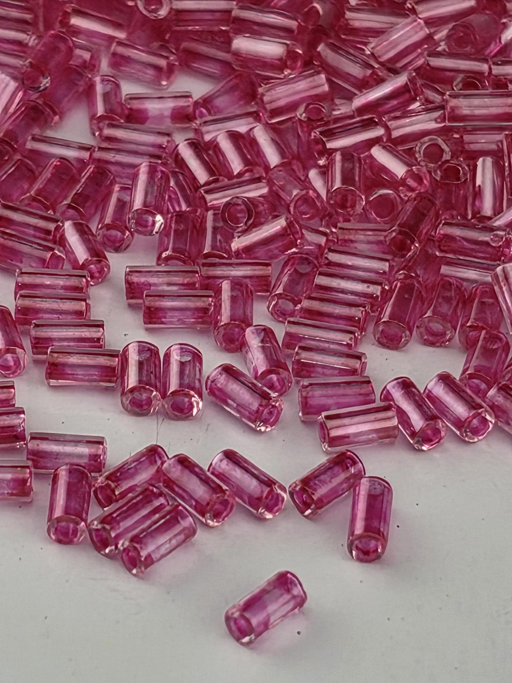 A close-up image of numerous small, clear beads in a vibrant shade of pink, scattered across a white surface.